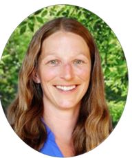 Middle aged white woman smiling at camera with leaves in background.